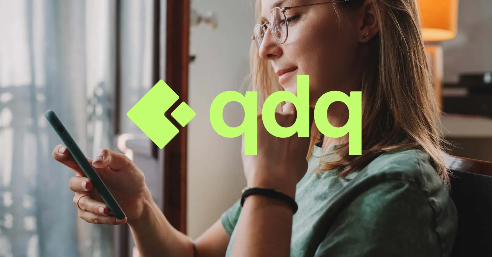 Mujer sonriendo ante su móvil con el logotipo verde de qdq sobre la foto.