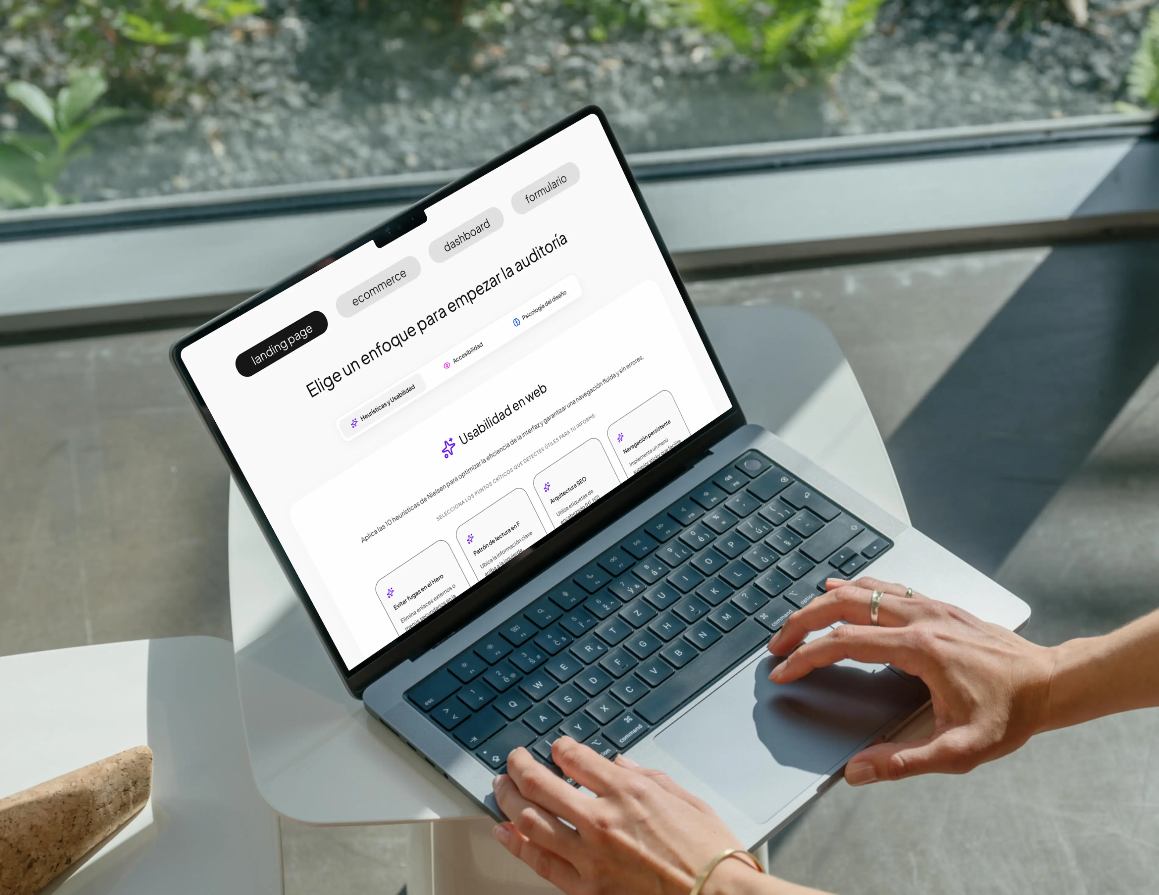 Persona escribiendo en un portátil en una sala luminosa; la pantalla muestra UX QuickAudit pidiendo elegir un enfoque de auditoría para un producto web.